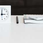 white desk clock near pen and book